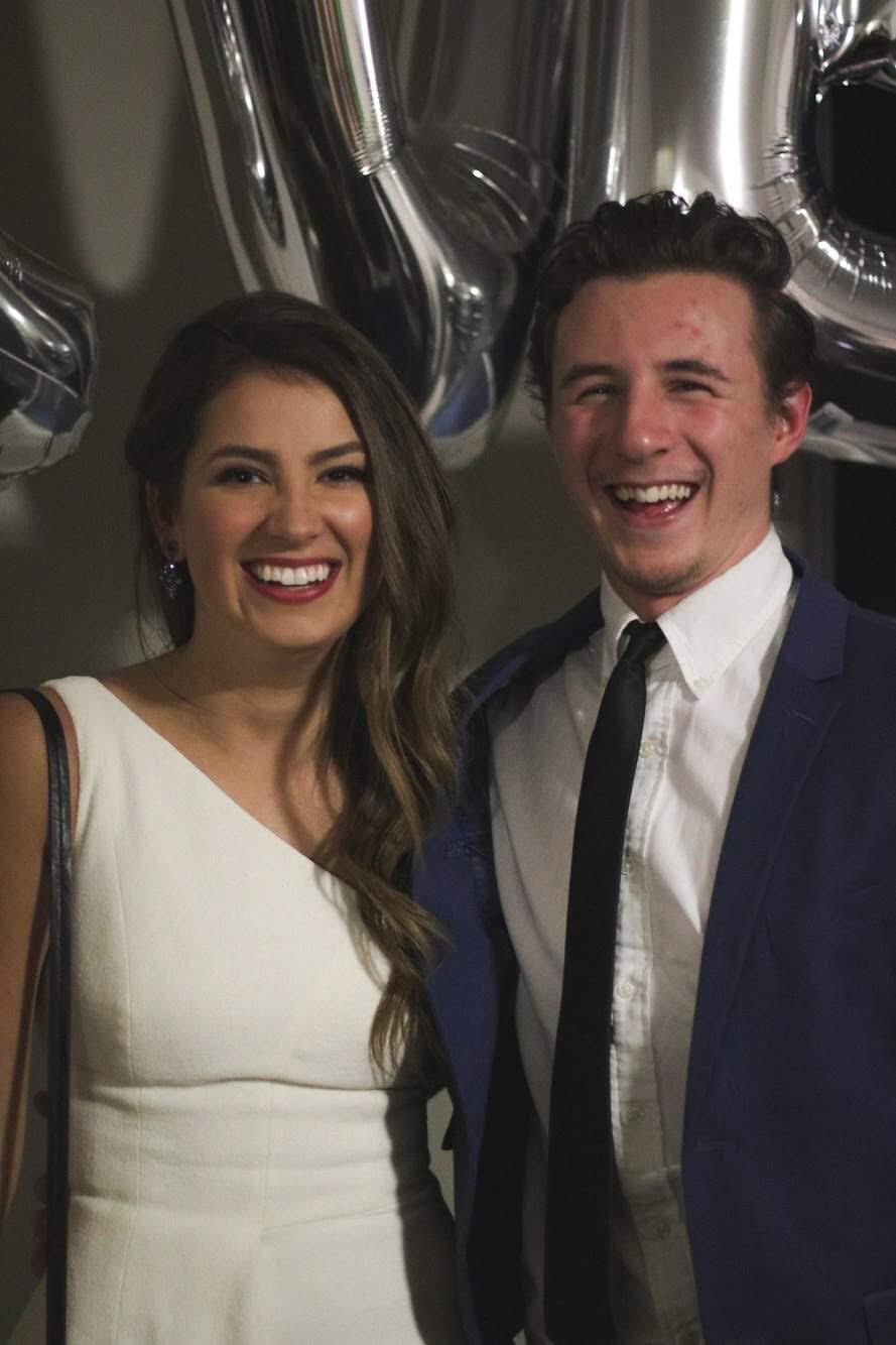 Mary and Hunter dressed up and laughing in front of a wall of silver balloons.