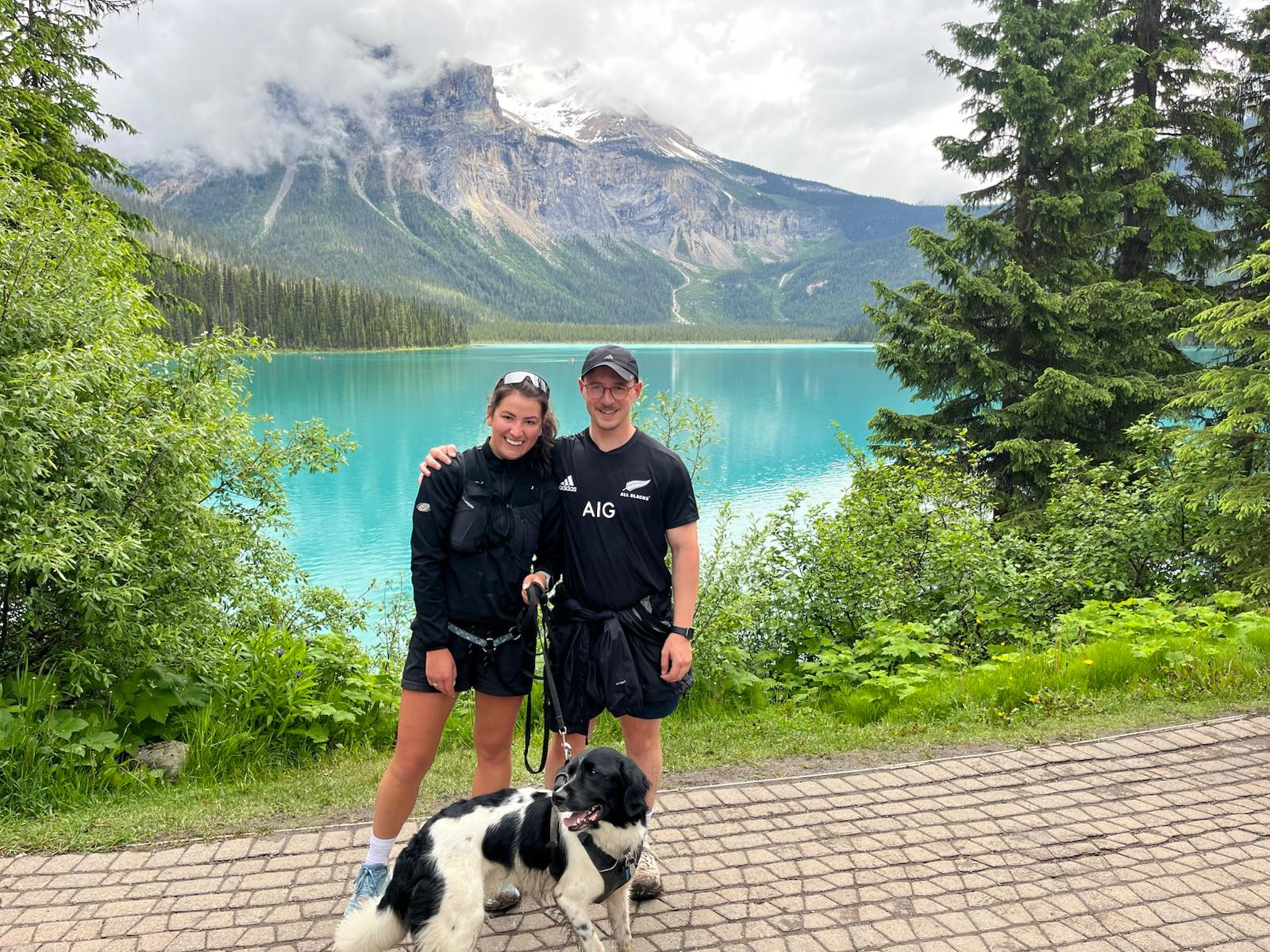 Mary and Hunter with their dog beside Emerald Lake, a cloud-covered peak behind them.